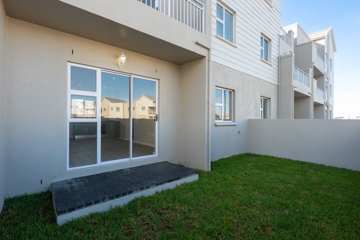 Rear view of the apartment featuring a private garden with a small paved patio area and sliding door access to the interior.