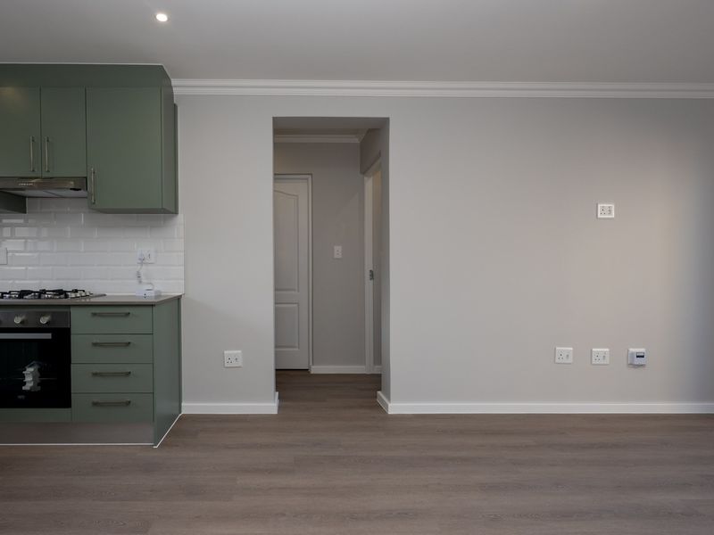 Modern open-plan living area featuring a sleek green kitchen with built-in appliances, subway tile backsplash, and durable laminate flooring throughout.