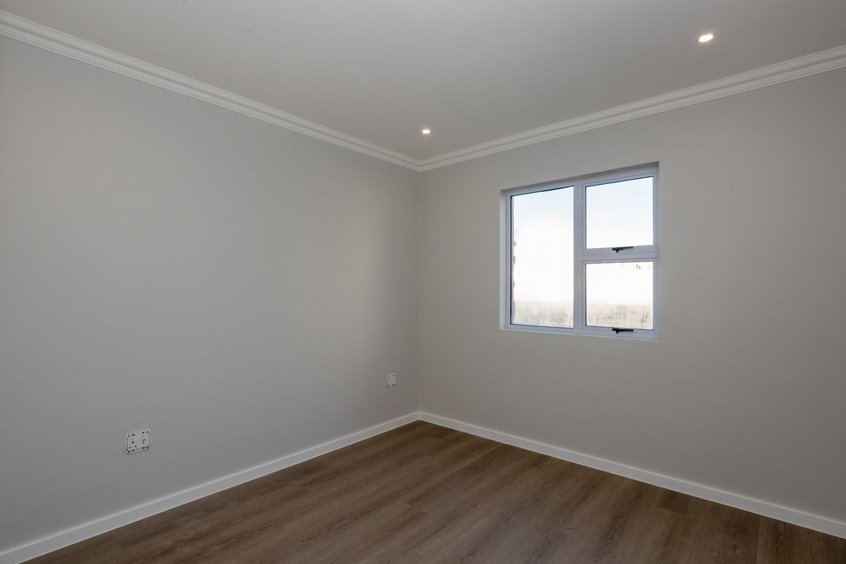 A clean, neutral bedroom featuring modern laminate flooring, recessed downlighting, and crisp white cornicing, providing a blank canvas for interior design.