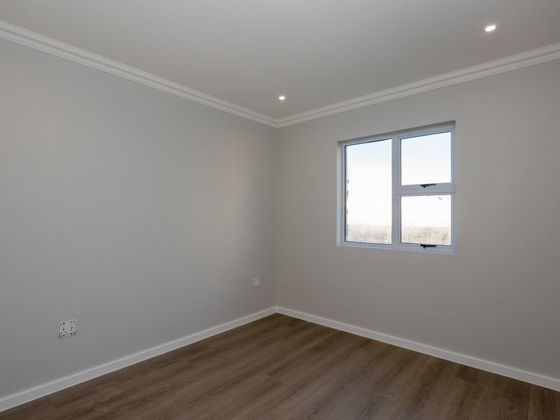 A clean, neutral bedroom featuring modern laminate flooring, recessed downlighting, and crisp white cornicing, providing a blank canvas for interior design.