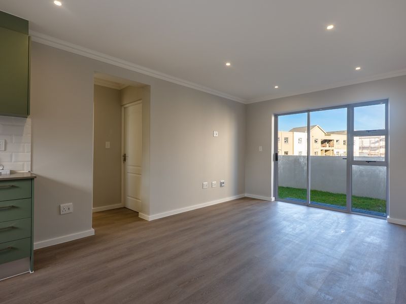 Modern open-plan living area featuring a sleek kitchen with green cabinetry, subway tile backsplash, and direct access to a private outdoor space.