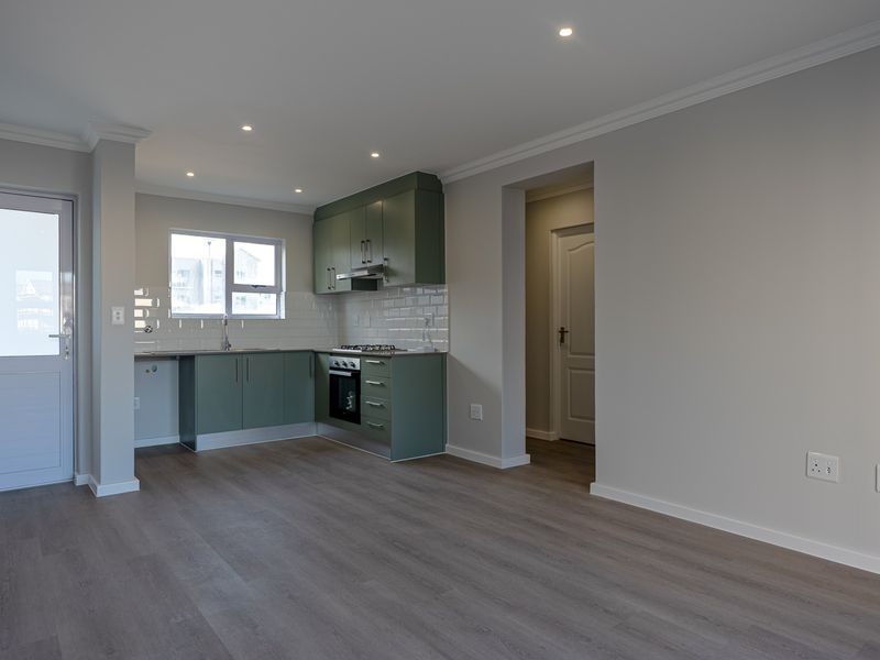 Modern open-plan living area featuring a sleek kitchen with green cabinetry, subway tile backsplash, integrated appliances, and durable laminate flooring throughout.