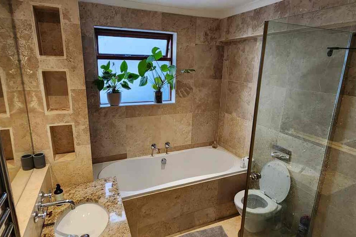 A well-appointed bathroom featuring travertine tiling, a built-in bathtub, a separate glass-enclosed shower, and a granite-topped vanity with integrated storage niches.