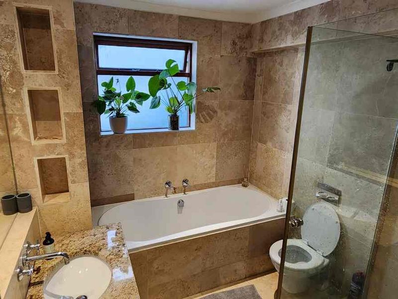 A well-appointed bathroom featuring travertine tiling, a built-in bathtub, a separate glass-enclosed shower, and a granite-topped vanity with integrated storage niches.
