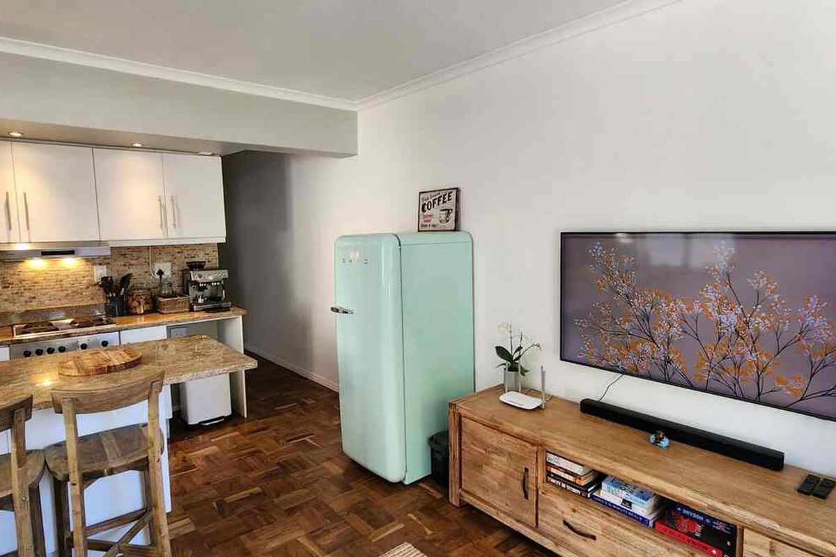 Open-plan living area featuring a compact kitchen with granite countertops, tiled backsplash, and warm parquet flooring throughout the combined space.