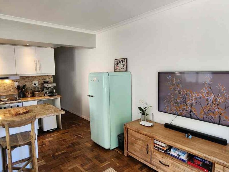 Open-plan living area featuring a compact kitchen with granite countertops, tiled backsplash, and warm parquet flooring throughout the combined space.