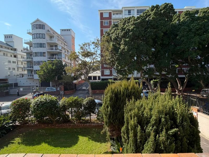 An elevated view overlooking a landscaped garden area with mature trees and surrounding apartment buildings in a residential neighborhood.