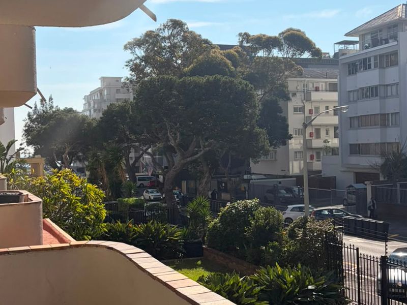 A view from a balcony overlooking a suburban street with mature trees and surrounding apartment buildings.