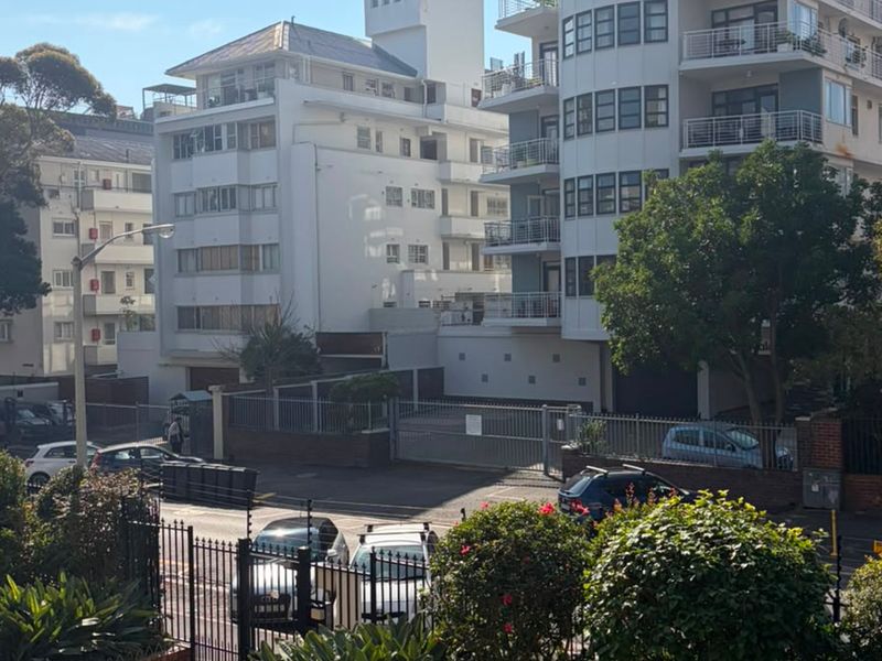 A street-level view of a multi-story apartment complex featuring secure gated access and residential balconies.