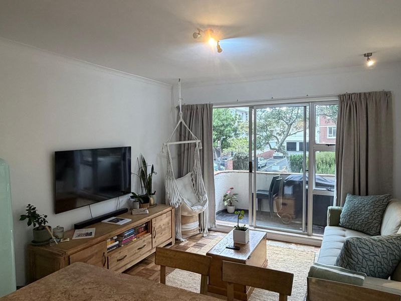 A bright living room featuring parquet flooring, coved ceilings, and large sliding glass doors that provide access to an outdoor balcony area.