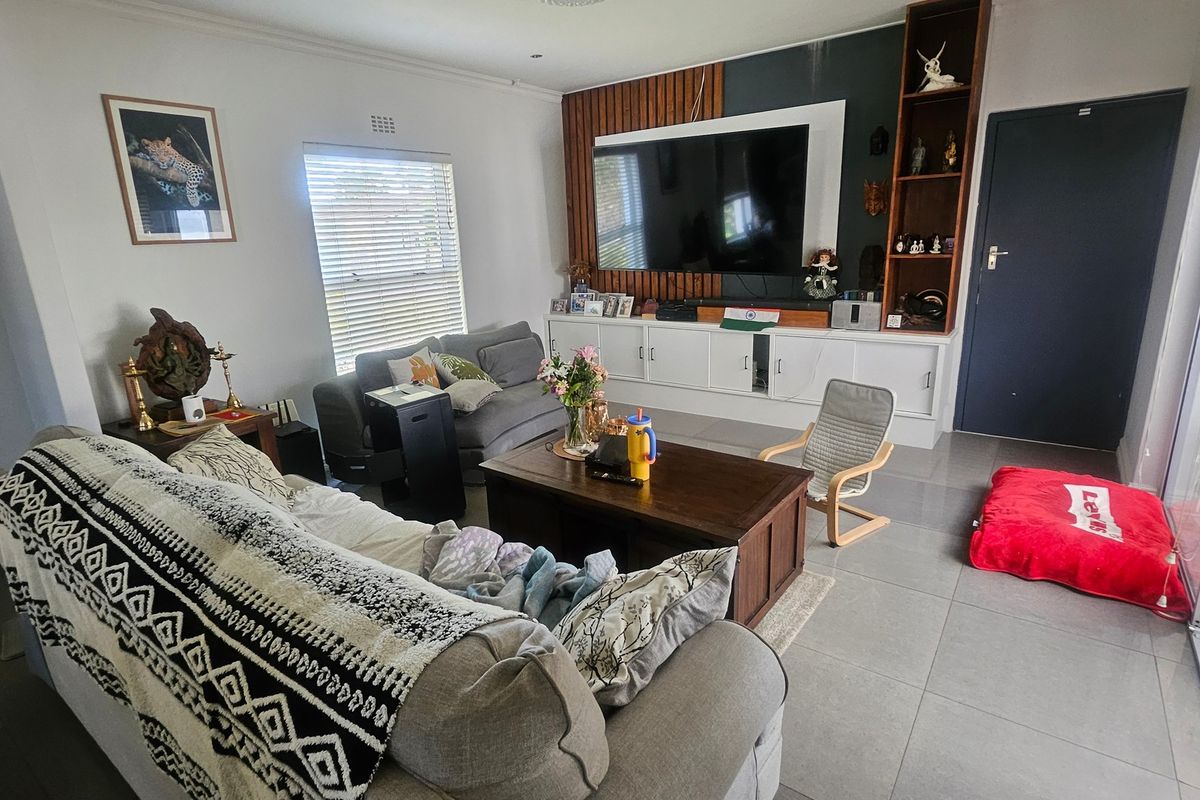 A comfortable living room featuring tiled flooring, a custom built-in media unit with slatted wood detailing, and direct access to the outdoor area.