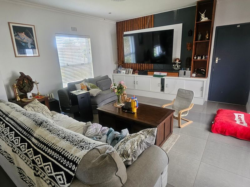 A comfortable living room featuring tiled flooring, a custom built-in media unit with slatted wood detailing, and direct access to the outdoor area.