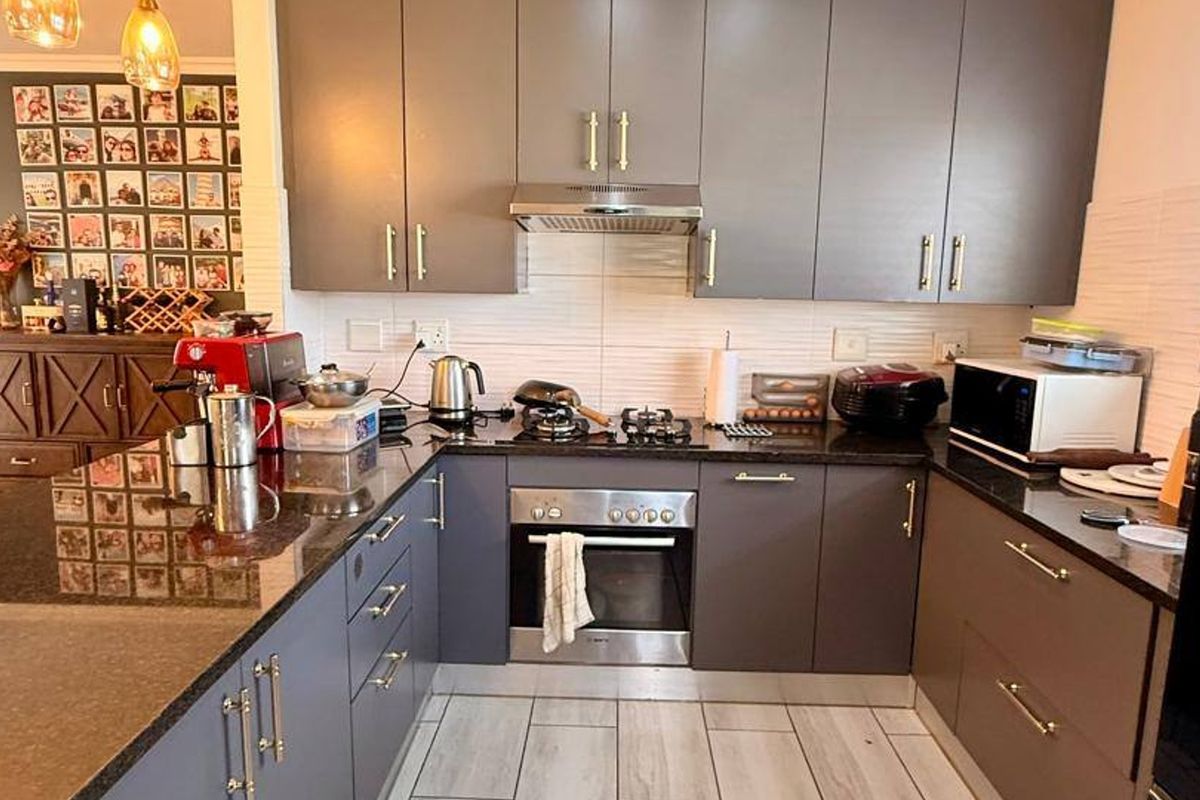 A modern kitchen featuring dark grey cabinetry, granite countertops, a stainless steel oven, gas hob, and extractor fan with light-toned tiled flooring.