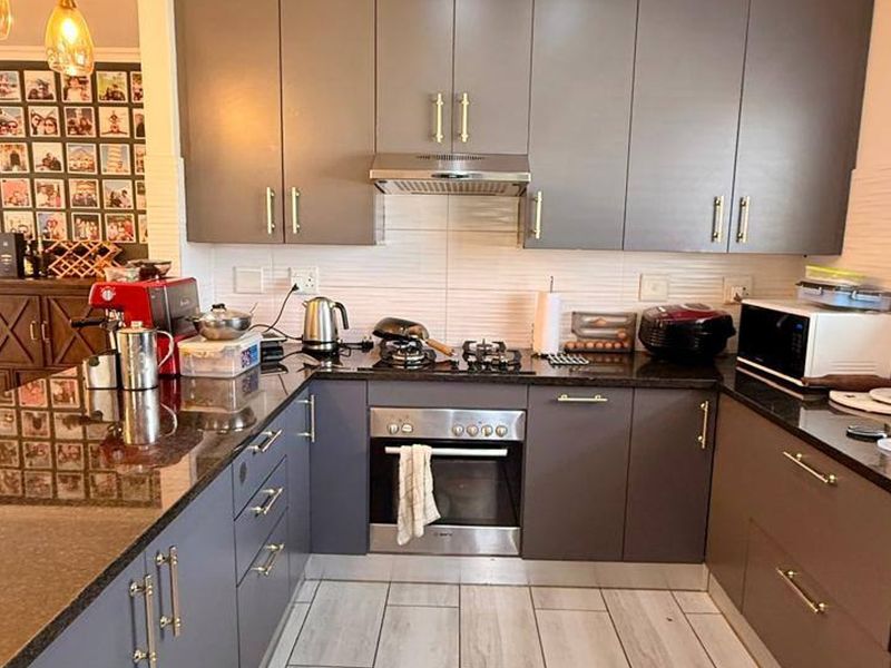 A modern kitchen featuring dark grey cabinetry, granite countertops, a stainless steel oven, gas hob, and extractor fan with light-toned tiled flooring.