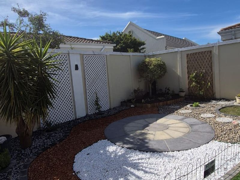 A well-maintained low-maintenance garden featuring a circular paved patio area, decorative gravel, and perimeter boundary walls with lattice screening.