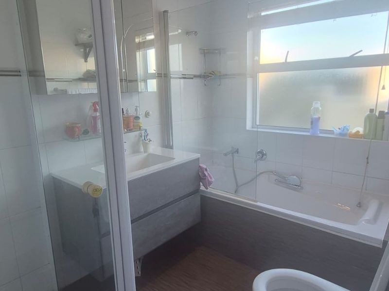 A functional bathroom featuring a modern vanity, a combined bathtub and shower enclosure, and a toilet, finished with tiled walls and a frosted window.