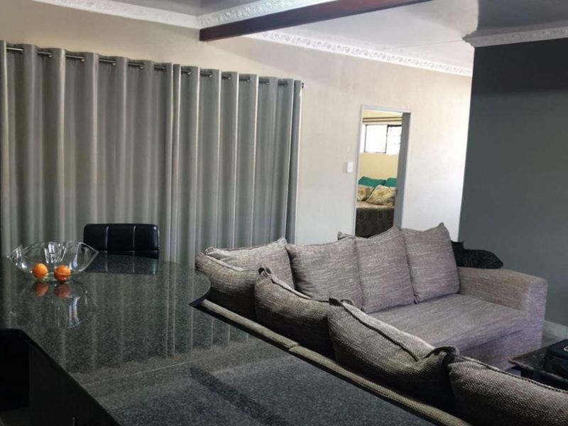 Open plan living area featuring a granite breakfast bar, decorative ceiling cornices, and an exposed beam, connecting to adjacent living and bedroom spaces.