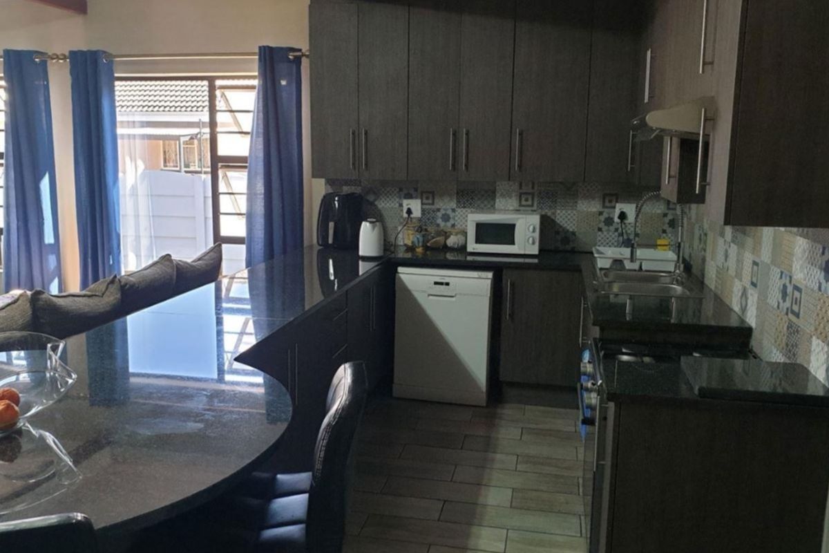 Modern kitchen featuring dark wood cabinetry, granite countertops, a breakfast bar, and a decorative patterned tile backsplash with tiled flooring.