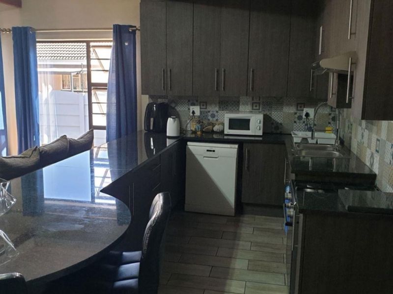 Modern kitchen featuring dark wood cabinetry, granite countertops, a breakfast bar, and a decorative patterned tile backsplash with tiled flooring.