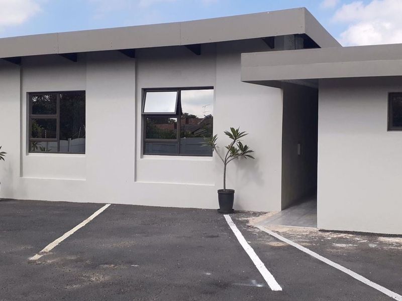 Front exterior view of the apartment building featuring a paved driveway, modern painted facade, and aluminium window frames.