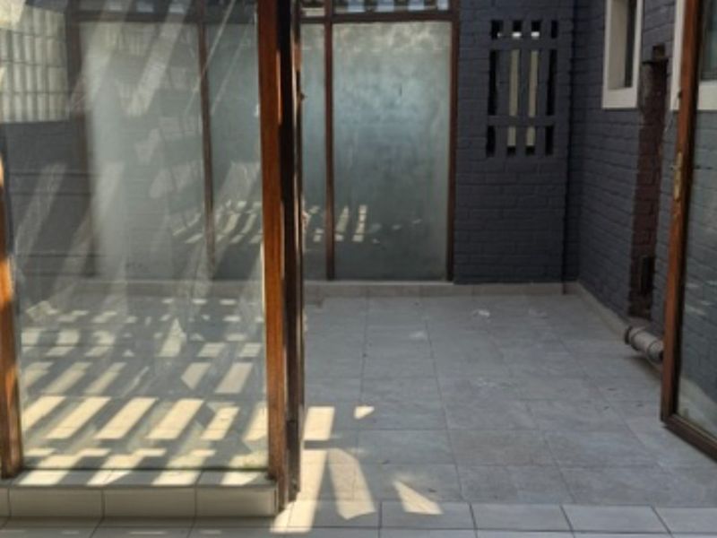 A covered patio area featuring tiled flooring, glass paneling, and painted brick walls, offering a versatile outdoor space.