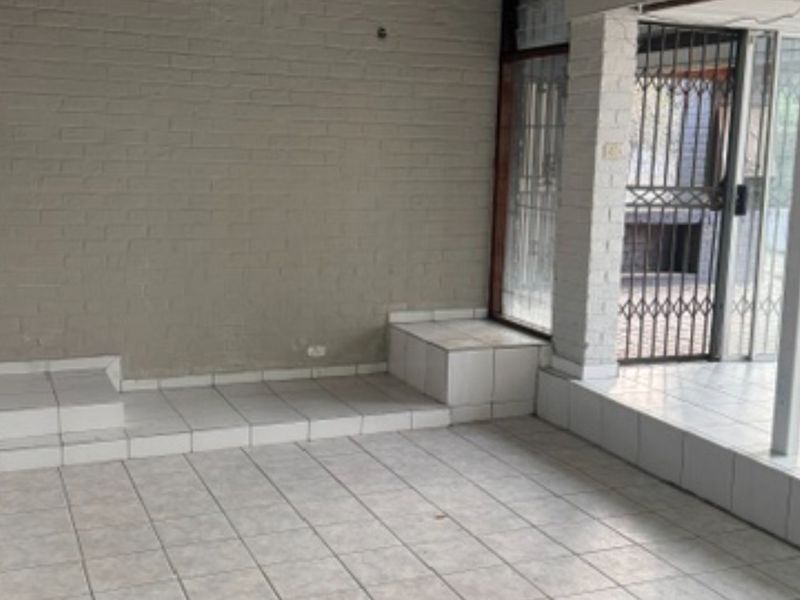 An empty covered patio area featuring tiled flooring, a raised platform, and a security gate leading to the outdoor space.
