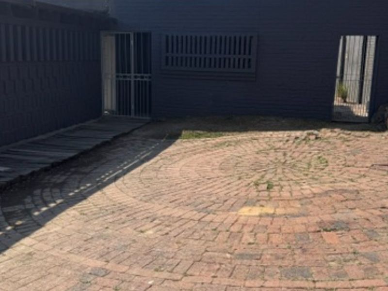 A rear courtyard area featuring circular brick paving, security gates, and painted brick walls, requiring maintenance to address weed growth and surface wear.