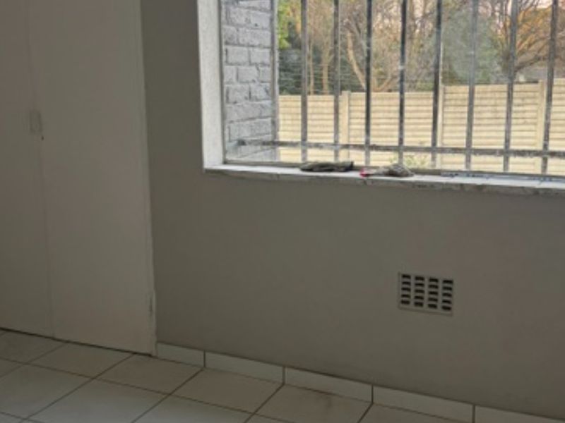 An empty bedroom featuring tiled flooring, built-in cupboards, and a window fitted with security bars.