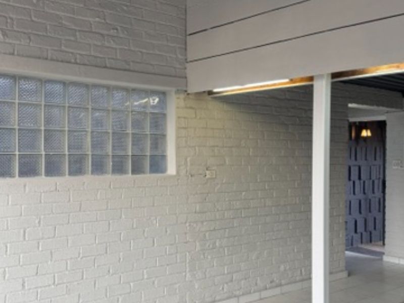 A covered outdoor patio area featuring painted brick walls, a glass block window, and tiled flooring, providing a clean and functional transition space.