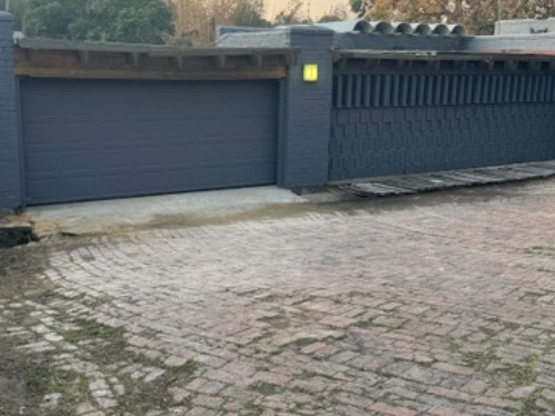 Front exterior view featuring a dark painted brick facade, a secure garage door, and a paved brick driveway.