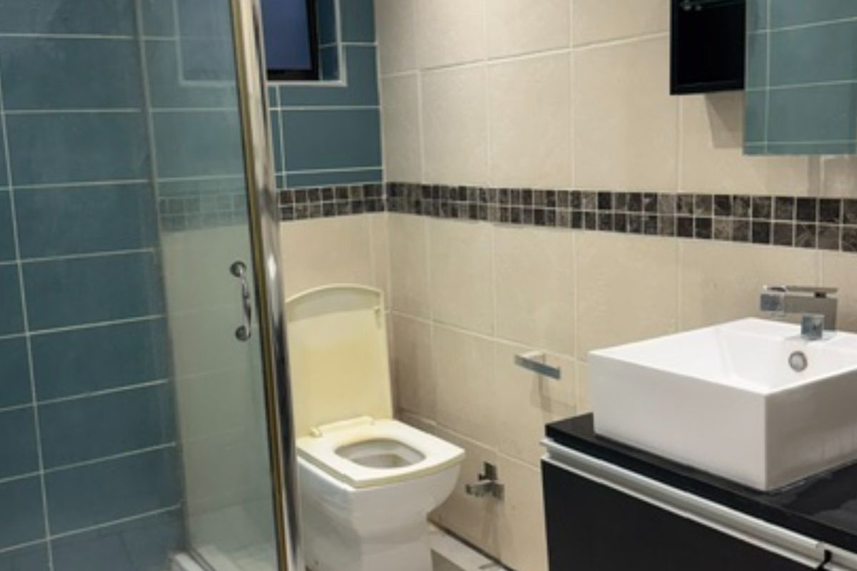 A functional bathroom featuring a glass shower enclosure, a modern vessel sink on a vanity cabinet, and tiled walls with a decorative mosaic border.