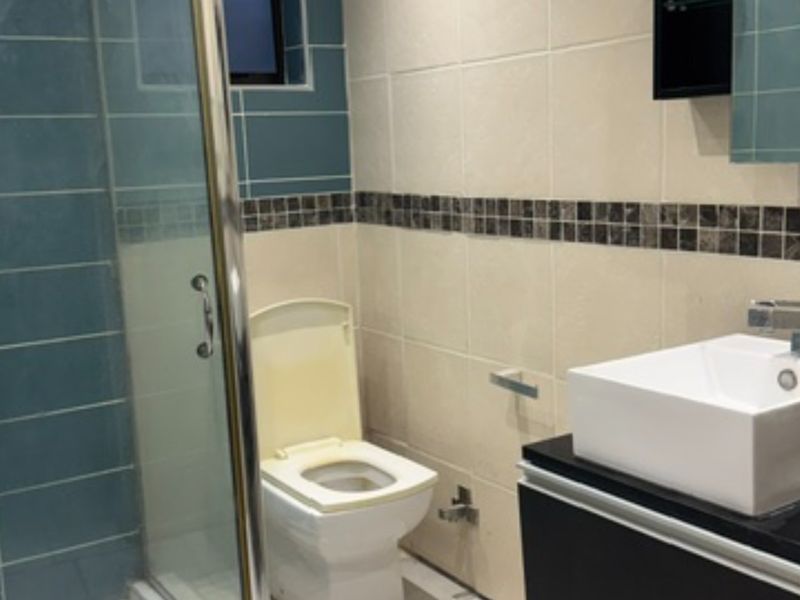 A functional bathroom featuring a glass shower enclosure, a modern vessel sink on a vanity cabinet, and tiled walls with a decorative mosaic border.