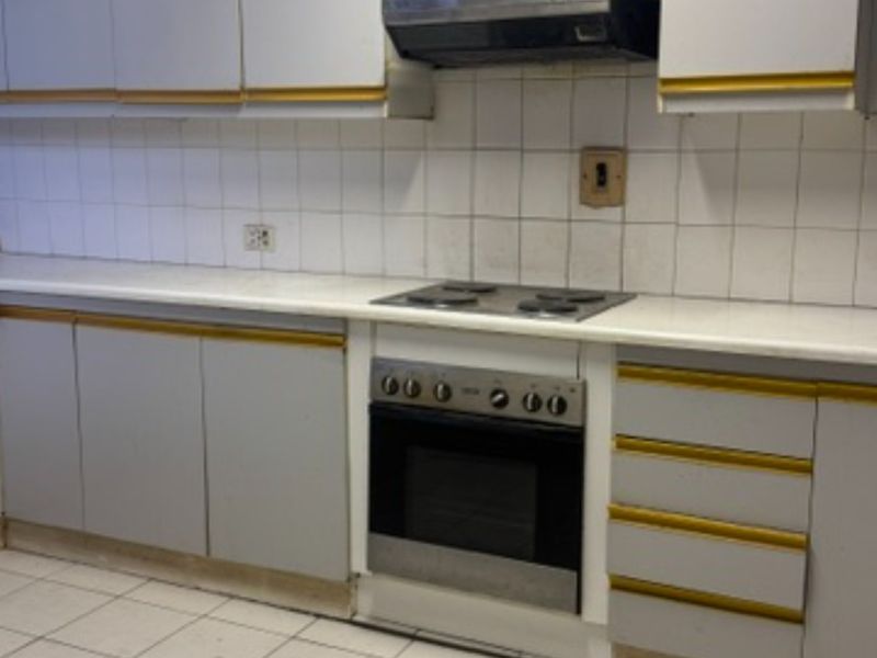 A dated kitchen featuring built-in cabinetry, an electric hob, an oven, and a tiled backsplash, offering a functional layout ready for modernization.