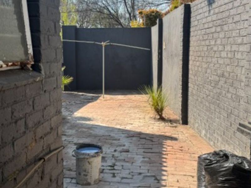 A private rear courtyard featuring painted brick boundary walls, brick paving, and a rotary clothesline, offering a blank canvas for outdoor landscaping.