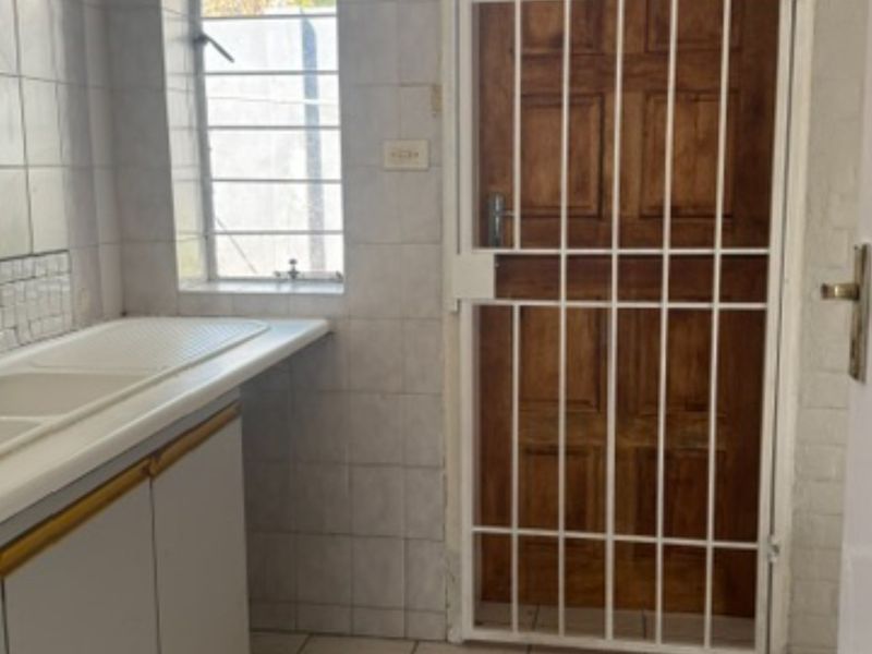 A functional scullery area featuring a double sink, tiled splashbacks, and a secure timber door with a fitted security gate.