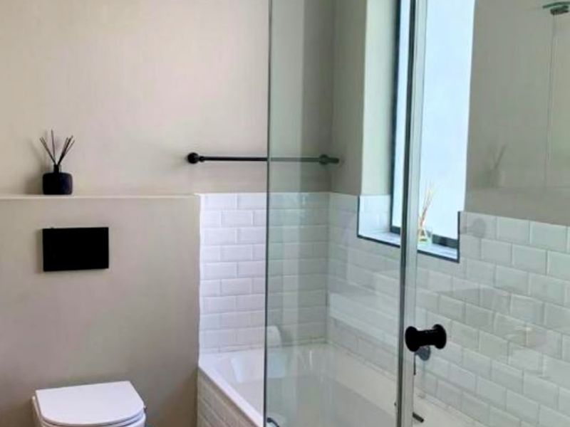 Modern bathroom featuring a wall-mounted toilet, subway tile accents, and a glass-enclosed bathtub with contemporary black fixtures.