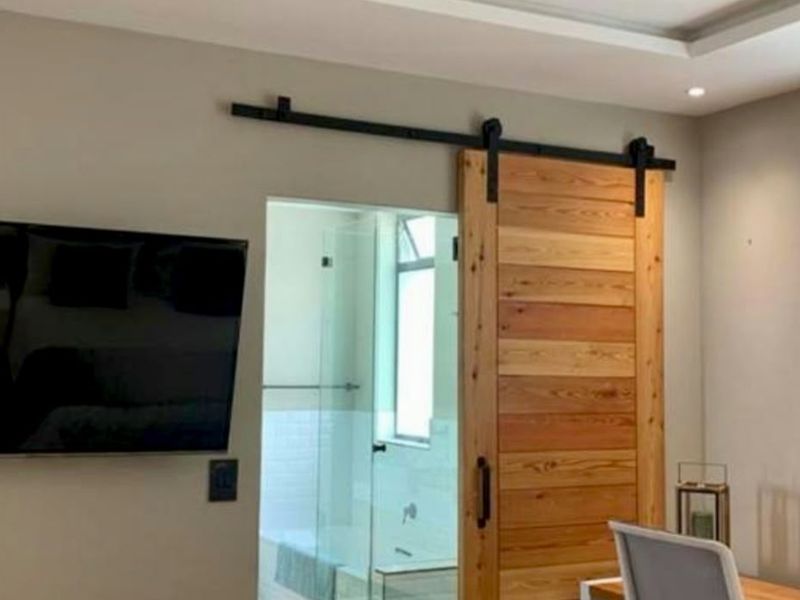 A modern bedroom featuring a wooden sliding barn door that provides access to an en-suite bathroom with a glass shower enclosure.