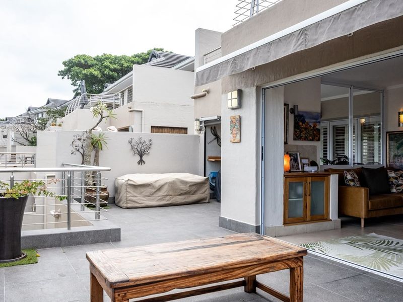 Spacious outdoor balcony featuring tiled flooring, a retractable awning, and stainless steel balustrades, providing seamless indoor-outdoor flow through large sliding glass doors.