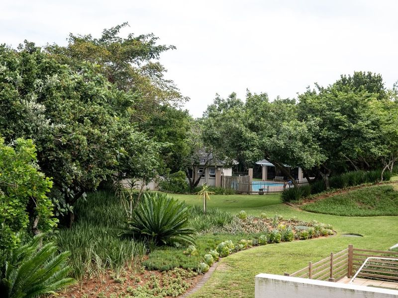 A well-maintained communal garden area featuring lush landscaping, mature trees, and a swimming pool visible in the background.