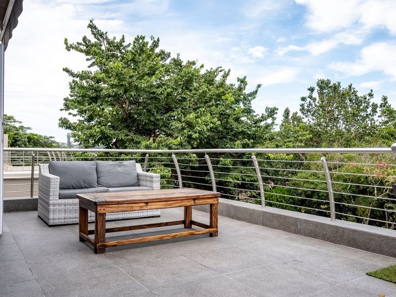 A spacious balcony featuring modern tiled flooring, a stainless steel balustrade, and a retractable awning, offering a pleasant outdoor living space.