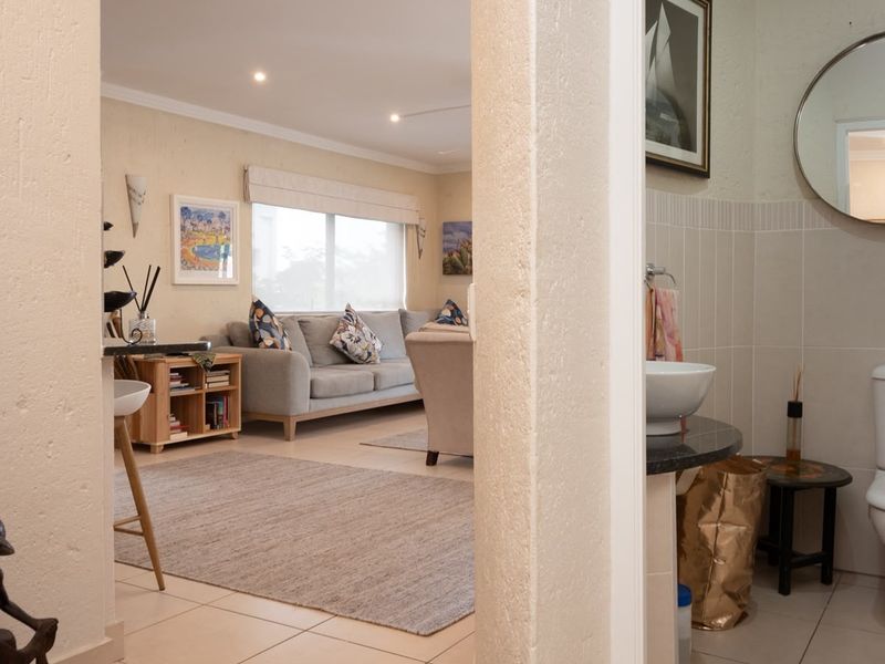 An open-plan living area featuring tiled floors and recessed lighting, adjacent to a compact bathroom with a modern vanity and toilet.