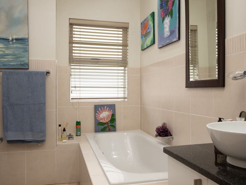 A well-maintained bathroom featuring a built-in bathtub, a modern vessel sink on a granite vanity, and neutral wall tiling.