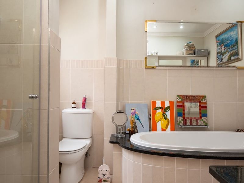 A well-maintained bathroom featuring a built-in bathtub with a granite surround, a separate shower enclosure, and neutral wall tiling.