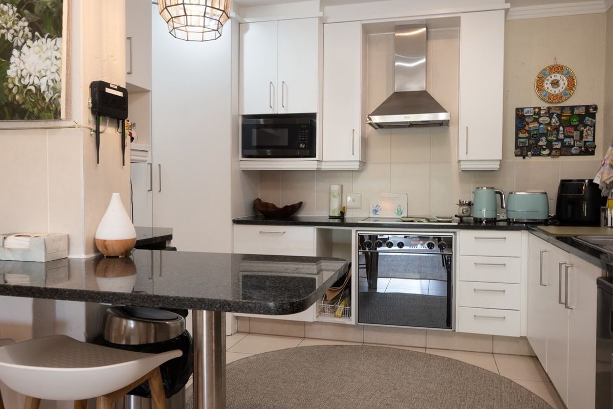A well-maintained kitchen featuring white cabinetry, granite countertops, a breakfast bar, and integrated stainless steel appliances including an oven and extractor fan.
