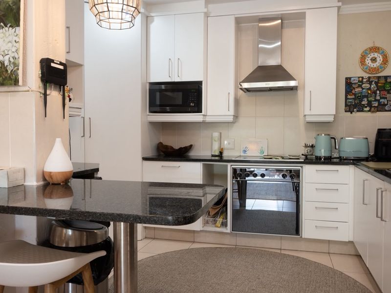 A well-maintained kitchen featuring white cabinetry, granite countertops, a breakfast bar, and integrated stainless steel appliances including an oven and extractor fan.