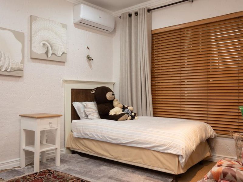 A well-maintained bedroom featuring textured walls, an integrated air conditioning unit, and wooden venetian blinds for privacy.