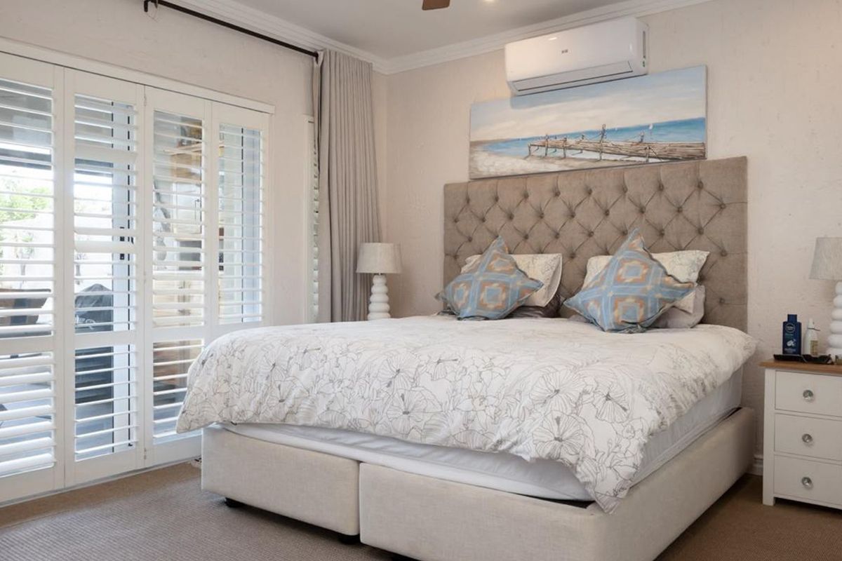 A well-maintained bedroom featuring neutral tones, plantation shutters, crown molding, and a wall-mounted split-system air conditioner.