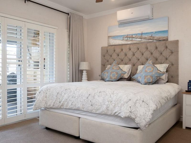 A well-maintained bedroom featuring neutral tones, plantation shutters, crown molding, and a wall-mounted split-system air conditioner.