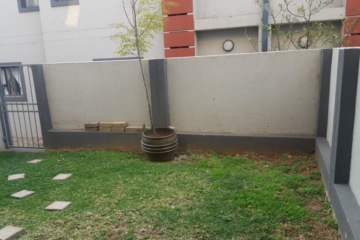 A private rear courtyard area featuring a lawn, boundary wall, and metal security gate access.