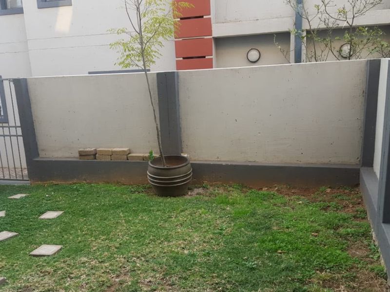 A private rear courtyard area featuring a lawn, boundary wall, and metal security gate access.